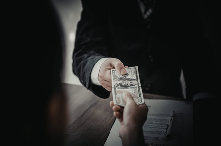 A man in a suit is handing over a stack of cash to another person in a dark setting.