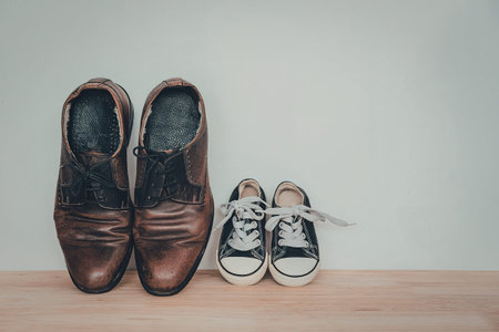 a pair of brown leather dress shoes and a pair of black and white sneakers on a wooden floorの写真素材