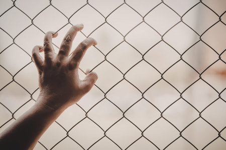 A hand reaching through a chain link fence with a blurred background.