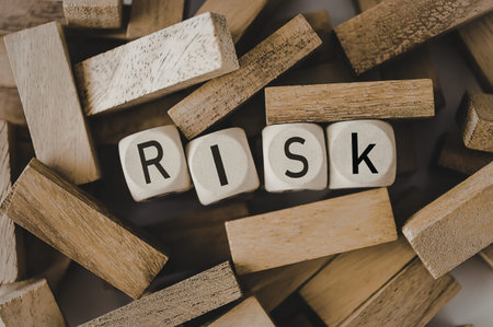 A close-up of wooden blocks with the word 'Risk' spelled out, surrounded by scattered blocks.