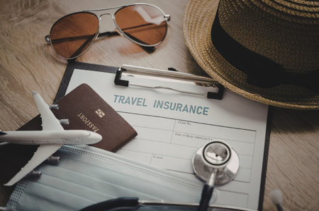 A travel insurance document on a clipboard with a passport, sunglasses, a hat, and a toy airplane.