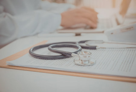 A stethoscope lies on a clipboard with a medical professional working in the background