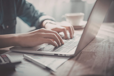 A person typing on a laptop keyboard with a cup of coffee in the background