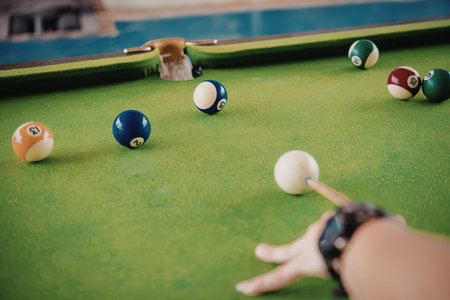 A person playing pool with a cue stick on a green felt table with multiple colored balls.