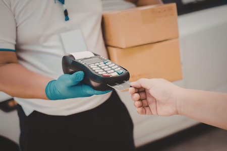 A person wearing blue gloves is holding a payment terminal and accepting a card from another person