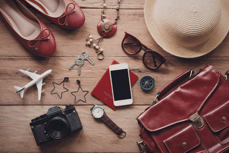 A collection of travel-related items including a red leather bag, shoes, hat, sunglasses, phone,...