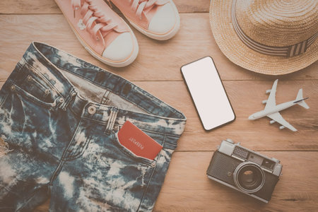 A collection of travel essentials including denim shorts, sneakers, a straw hat, a camera, a...