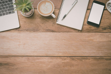 A wooden desk with a laptop, coffee cup, notebook, pen, and smartphone on it.