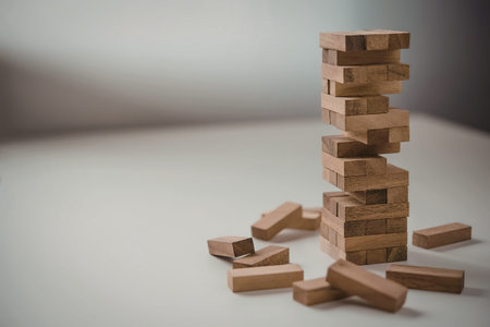 A stack of wooden blocks standing on a flat surface with some blocks scattered around the base, showcasing a precarious tower.の写真素材