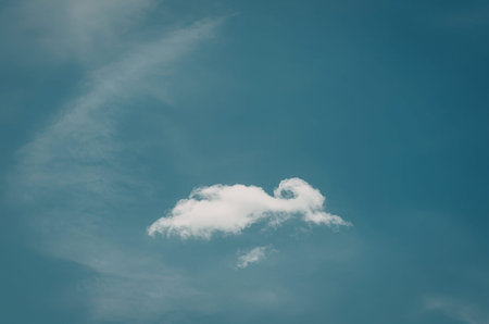 A single white cloud in a bright blue sky with wispy clouds