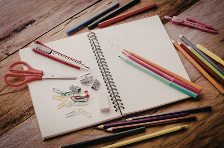 A spiral notebook with colorful pencils and pens scattered around it on a wooden table.