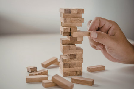A hand holding a wooden block, about to play with a tower made of wooden blocks.