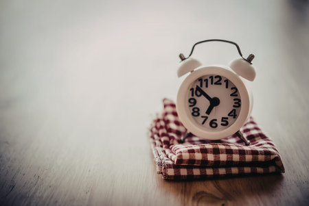 An alarm clock sitting on a red and white checkered cloth, placed on a wooden surface.