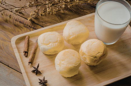 A wooden tray holding cheese, a glass of milk, cinnamon sticks, and star anise on a wooden table.