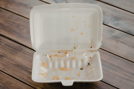 An open, empty food container with remnants of food on a wooden table.