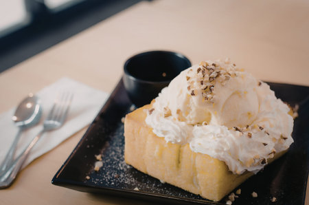 A slice of toast topped with whipped cream and nuts on a black plate.
