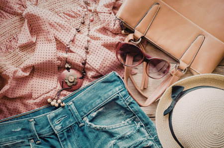 A stylish arrangement of summer clothing and accessories including a pink sweater, blue jeans, a tan...