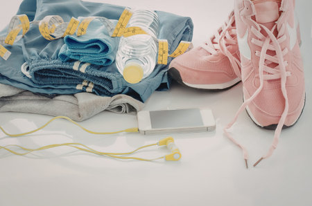 A pair of pink sneakers, a water bottle, a blue gym towel, and earbuds laid out on a white surface.