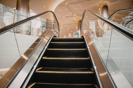 An empty escalator with black steps and yellow edges, surrounded by glass and metal railings, in a...