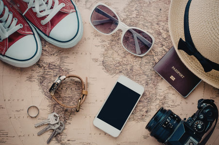 A collection of travel essentials including red sneakers, sunglasses, a straw hat, a passport, a...