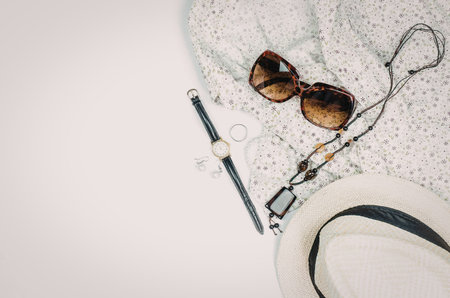 A flat lay of summer accessories including sunglasses, a straw hat, and a beaded cord.