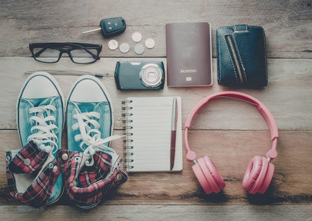 A collection of travel essentials including shoes, headphones, a camera, passport, and notebook laid...