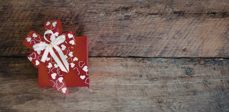 A red gift tag with a white ribbon and hearts on a wooden background