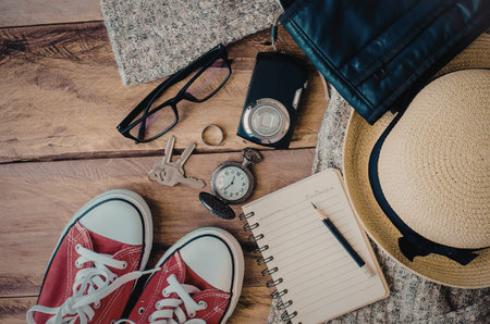 A collection of travel essentials including red sneakers, a straw hat, a notebook, and other...