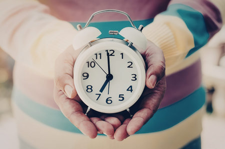 A person wearing a multicolored striped sweater holding an alarm clock in their hands.