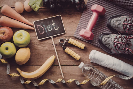 A flat lay of healthy food, fitness equipment, and measuring tape on a wooden table.