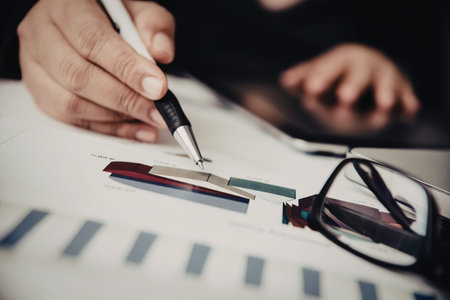 A person is analyzing data with a pen on a paper, with glasses and a blurred background.