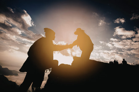 A silhouette of two people shaking hands against a vibrant sunset background with clouds and a...