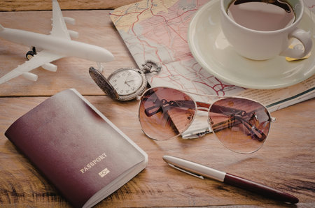 A collection of travel planning essentials including a passport, airplane model, watch, sunglasses,...