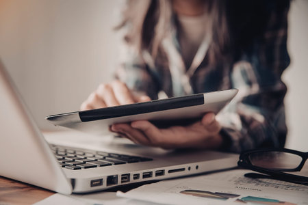 A woman working on a laptop with a pen and papers on the desk, possibly studying or working.