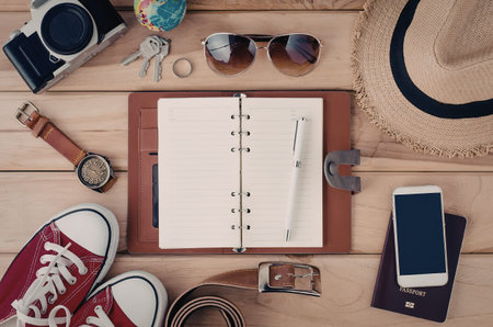 A collection of travel planning essentials including a notebook, camera, sunglasses, hat, and other...