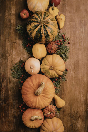 An arrangement of various pumpkins and fruits on a wooden surface, decorated with green leaves and...