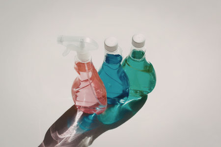 Three bottles of cleaning solution in red, blue, and green, with white caps and spray nozzles,...