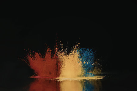A vibrant explosion of red, yellow, and blue powder on a black background, with a reflection below.