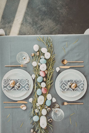 An overhead view of a table set for Easter with pastel colored eggs and greenery as centerpiece