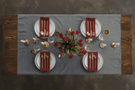 Overhead view of a beautifully set dining table with red napkins, plates, and flowers on a gray...