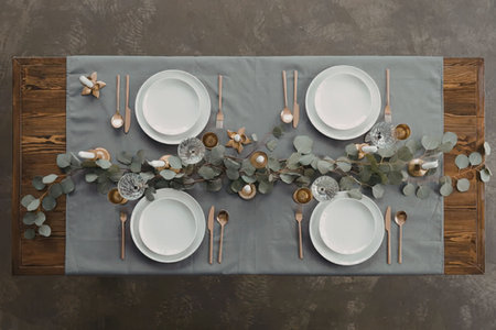 An overhead view of a beautifully set table with a eucalyptus centerpiece, white plates, and gold...