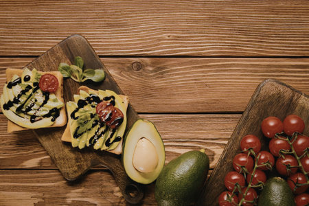 A wooden board with avocado toast, cherry tomatoes, and fresh ingredients on a rustic wood...