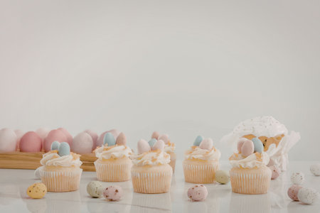 A row of cupcakes with white frosting and decorated with small colorful eggs on top, surrounded by...