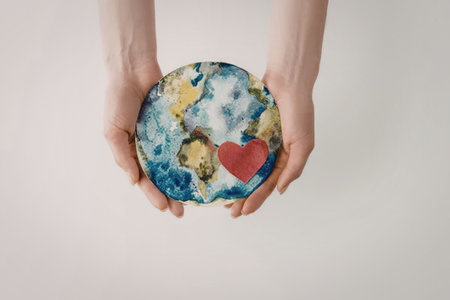 A pair of hands gently holding a globe with a red heart symbolizing love and care for the planet.