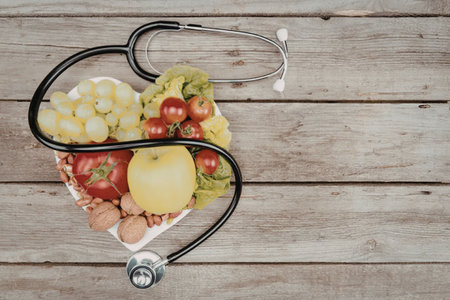 A stethoscope forming a heart shape with fresh fruits and vegetables on a wooden background