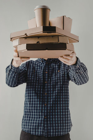 A man wearing a blue plaid shirt holding a stack of cardboard food boxes and a cup