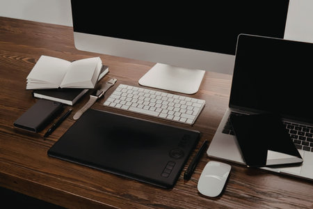A modern workspace with a laptop, keyboard, mouse, monitor, notebook, and a graphics tablet on a...