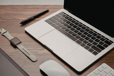 A modern workspace setup featuring a laptop, wireless mouse, keyboard, smartwatch, and pen on a...