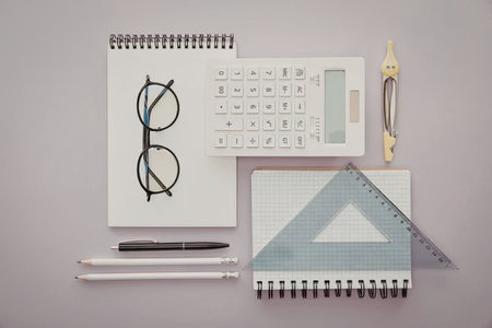 A collection of office supplies including notebooks, pens, glasses, and a ruler on a purple...