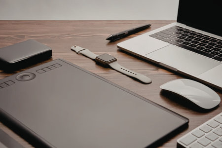 A well-organized workspace featuring a laptop, mousepad, mouse, keyboard, smartwatch, and stylus on...